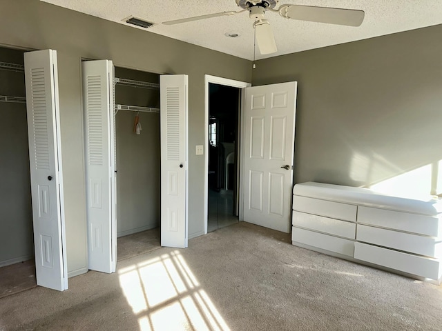 unfurnished bedroom with a textured ceiling, visible vents, two closets, and light colored carpet