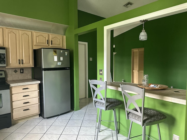 kitchen with tile countertops, lofted ceiling, appliances with stainless steel finishes, hanging light fixtures, and a kitchen bar