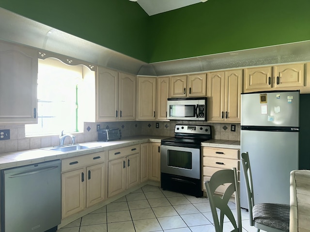 kitchen with light tile patterned floors, a sink, appliances with stainless steel finishes, tile counters, and tasteful backsplash