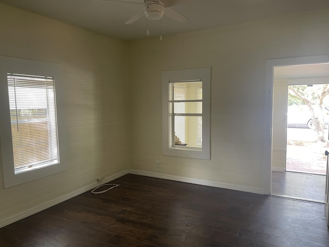 spare room featuring a healthy amount of sunlight, dark wood-style floors, baseboards, and a ceiling fan