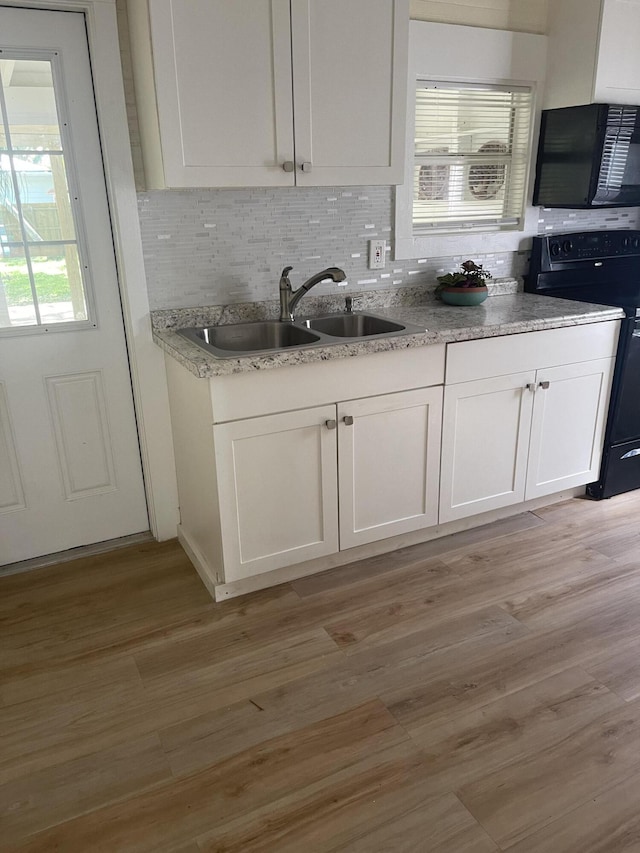 kitchen featuring light wood-style floors, black range with electric stovetop, white cabinets, and a sink