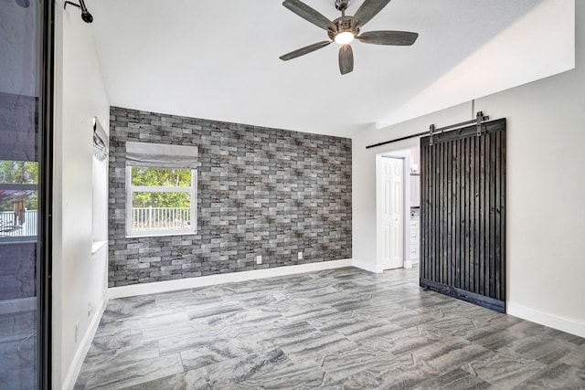 spare room featuring a barn door, a ceiling fan, brick wall, an accent wall, and vaulted ceiling