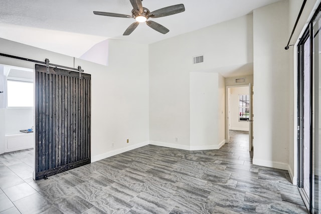 spare room with a barn door, visible vents, baseboards, lofted ceiling, and ceiling fan