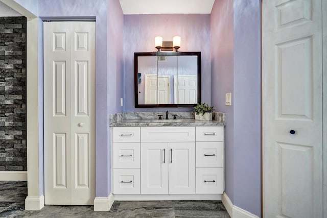 bathroom with a closet, a tile shower, vanity, and baseboards