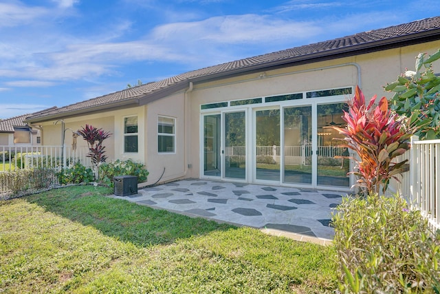 rear view of house featuring a tiled roof, fence, a yard, a patio area, and stucco siding