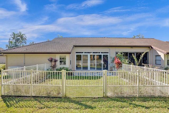 rear view of property with a tiled roof, a fenced front yard, a lawn, and stucco siding