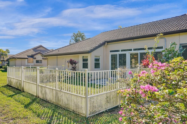 rear view of property featuring a yard, a tile roof, fence, and stucco siding
