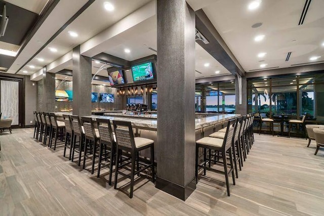 bar with a community bar, ornate columns, wood finished floors, and recessed lighting