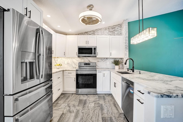 kitchen with a peninsula, a sink, vaulted ceiling, appliances with stainless steel finishes, and light stone countertops