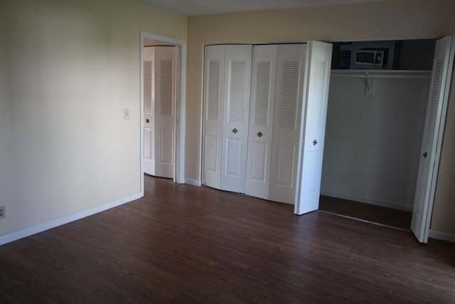 unfurnished bedroom featuring multiple closets, dark wood-style flooring, and baseboards