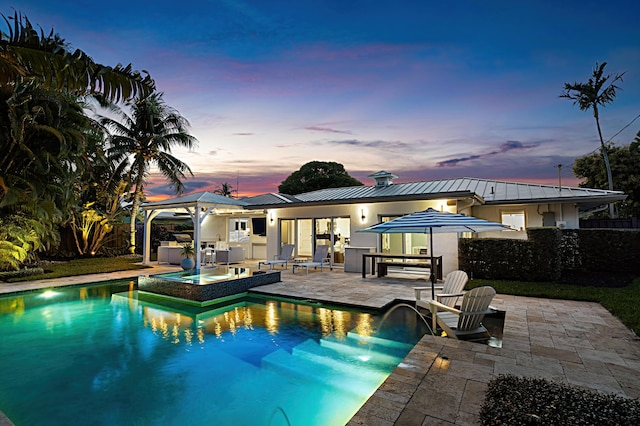 pool at dusk with a fenced in pool, area for grilling, a patio area, a fenced backyard, and a jacuzzi