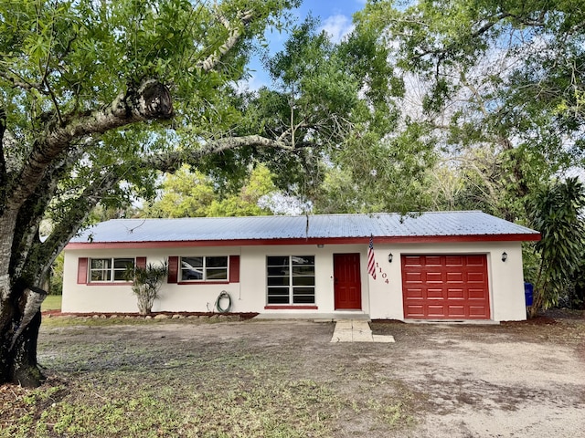 ranch-style house with a garage, driveway, metal roof, and stucco siding