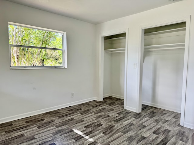 unfurnished bedroom featuring dark wood-style floors, baseboards, and multiple closets