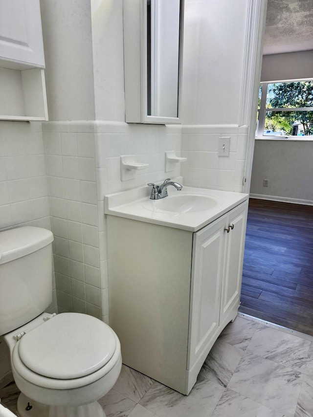 bathroom with marble finish floor, tile walls, toilet, vanity, and a textured ceiling