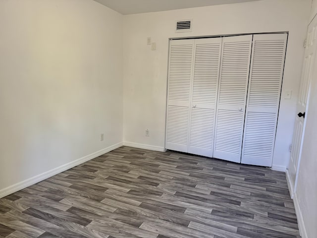 unfurnished bedroom featuring dark wood-style floors, a closet, visible vents, and baseboards