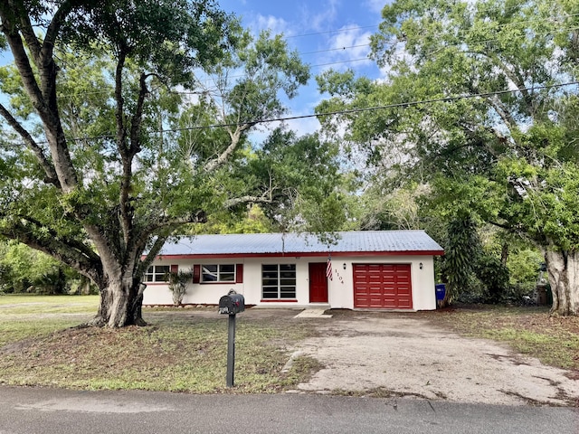 single story home with a garage, metal roof, driveway, and stucco siding