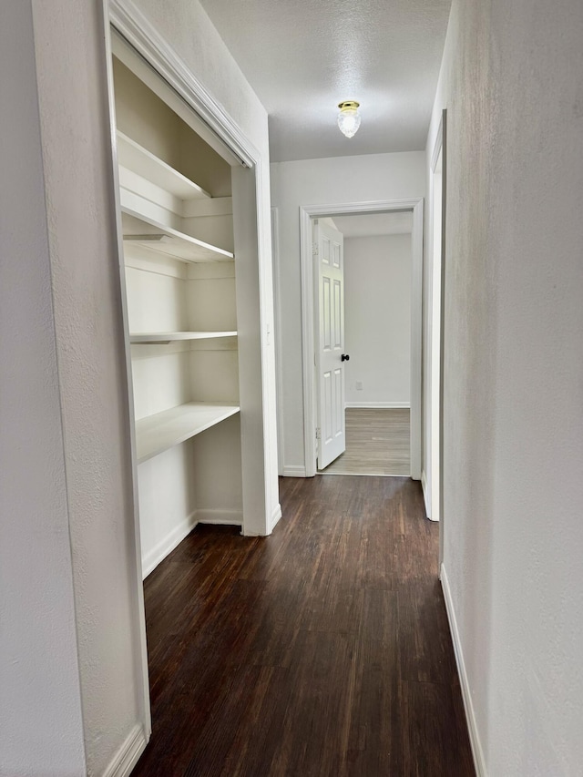 hallway featuring dark wood-style flooring and baseboards