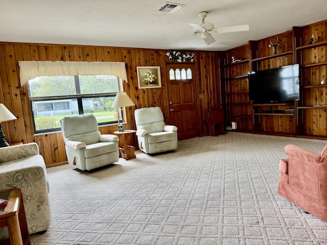 living area with wood walls, carpet, visible vents, and a ceiling fan