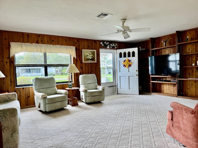 unfurnished living room featuring a ceiling fan, light colored carpet, wood walls, and visible vents