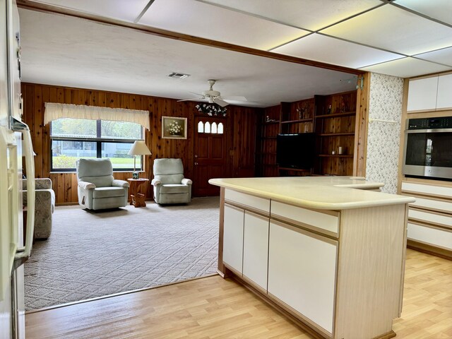 kitchen with light wood finished floors, a ceiling fan, open floor plan, oven, and light countertops