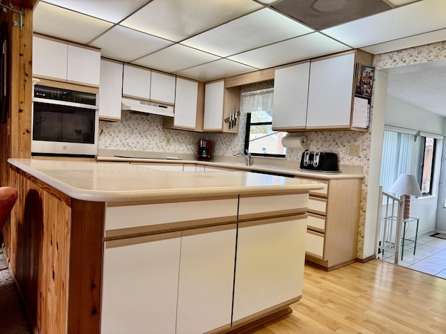 kitchen with light countertops, light wood-style floors, white cabinetry, oven, and under cabinet range hood