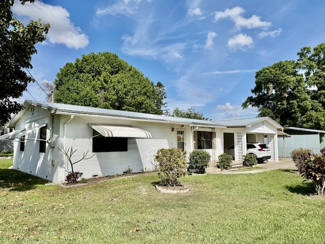 view of front facade with a carport, a front yard, concrete block siding, and metal roof