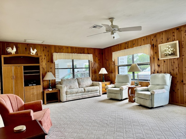 living area featuring a ceiling fan, light colored carpet, visible vents, and wood walls