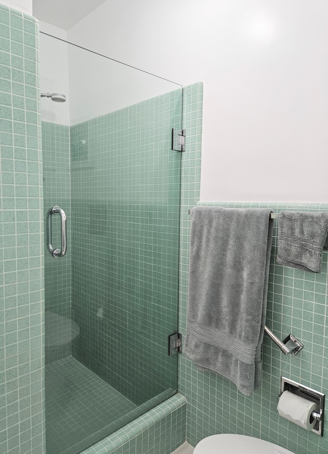 bathroom featuring wainscoting, tiled shower, tile walls, and toilet