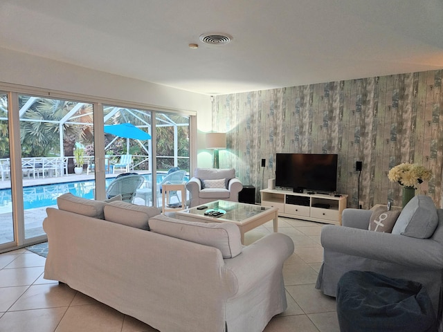 living room featuring a sunroom, wooden walls, visible vents, and light tile patterned flooring