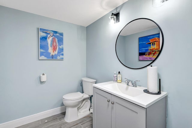 half bathroom featuring wood finish floors, baseboards, vanity, and toilet