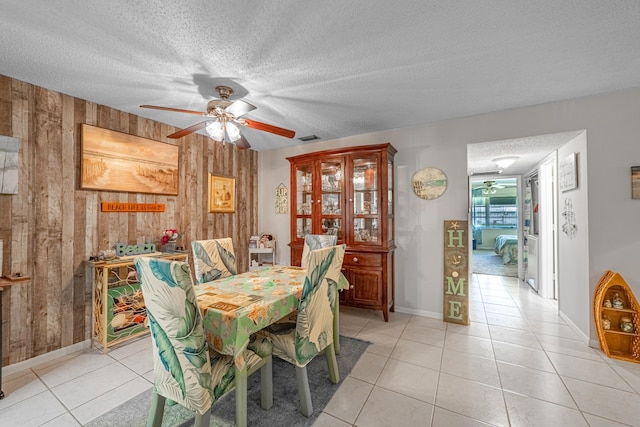 dining room with light tile patterned floors, visible vents, ceiling fan, a textured ceiling, and wood walls