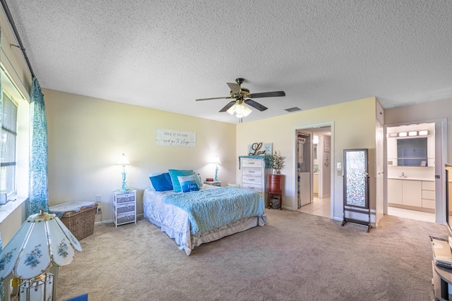 bedroom featuring light carpet, visible vents, ceiling fan, ensuite bathroom, and a textured ceiling