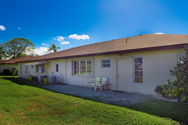 rear view of house with a patio, cooling unit, a lawn, roof with shingles, and stucco siding