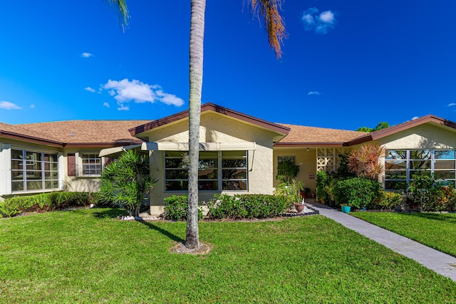 single story home featuring a front yard, roof with shingles, and stucco siding