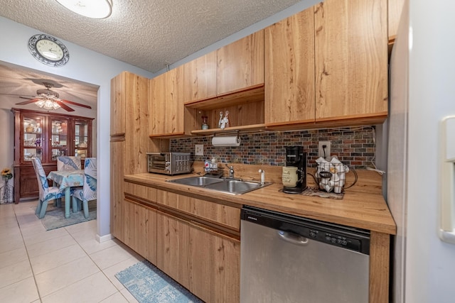 kitchen featuring light tile patterned floors, wooden counters, stainless steel dishwasher, freestanding refrigerator, and a sink