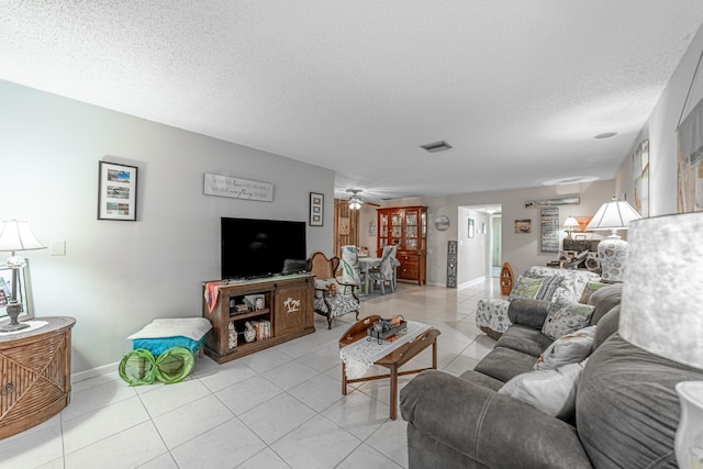 living area featuring light tile patterned floors, visible vents, ceiling fan, a textured ceiling, and baseboards