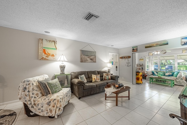 living area featuring light tile patterned floors, visible vents, ceiling fan, a textured ceiling, and baseboards