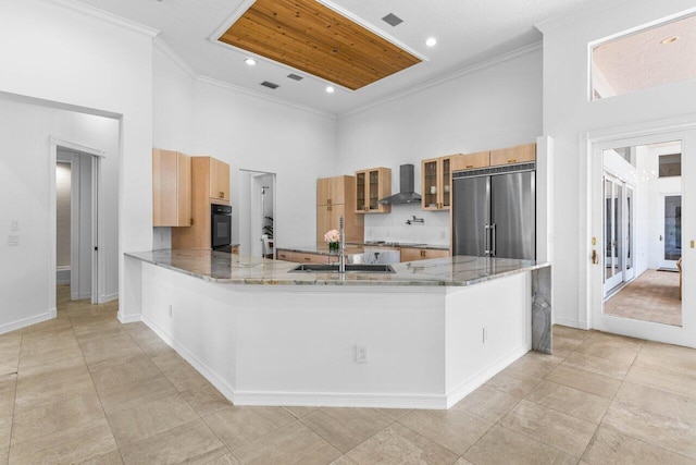 kitchen with oven, a peninsula, wall chimney range hood, stainless steel built in refrigerator, and glass insert cabinets