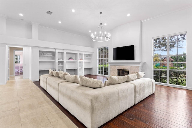 living room with visible vents, ornamental molding, wood finished floors, a chandelier, and a high end fireplace