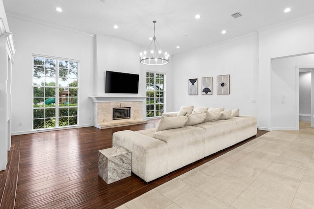 living area featuring crown molding, a notable chandelier, visible vents, a high end fireplace, and baseboards