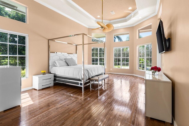 bedroom featuring baseboards, a tray ceiling, wood finished floors, and crown molding