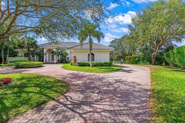 mediterranean / spanish house with a tiled roof, a front yard, decorative driveway, and stucco siding