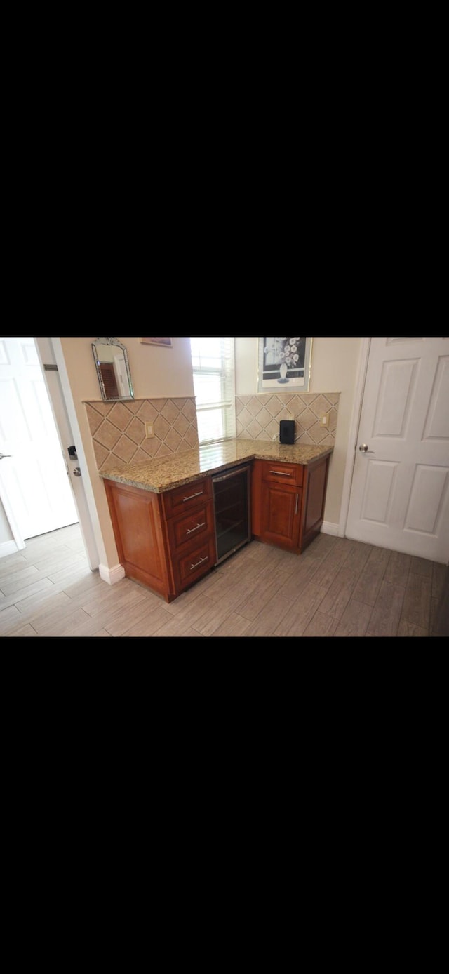 kitchen with beverage cooler, light wood finished floors, backsplash, and brown cabinets