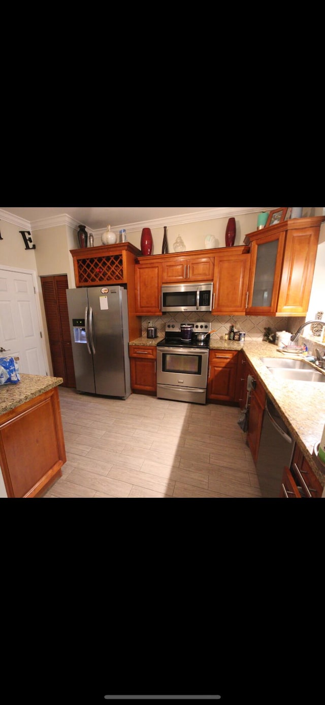 kitchen featuring light stone counters, a sink, appliances with stainless steel finishes, brown cabinetry, and glass insert cabinets