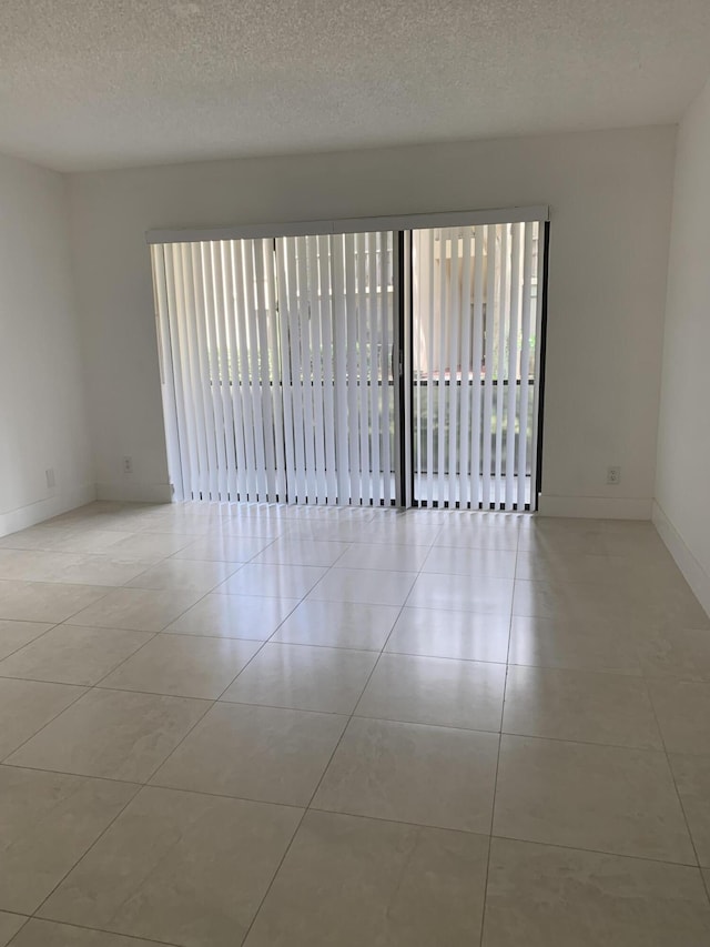 empty room featuring light tile patterned floors, a textured ceiling, and baseboards