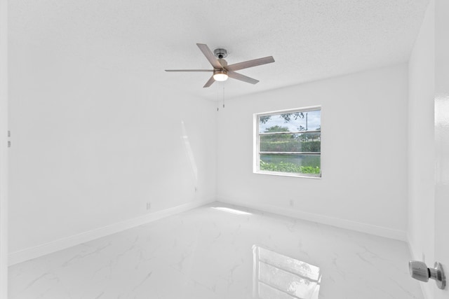 empty room with marble finish floor, ceiling fan, baseboards, and a textured ceiling