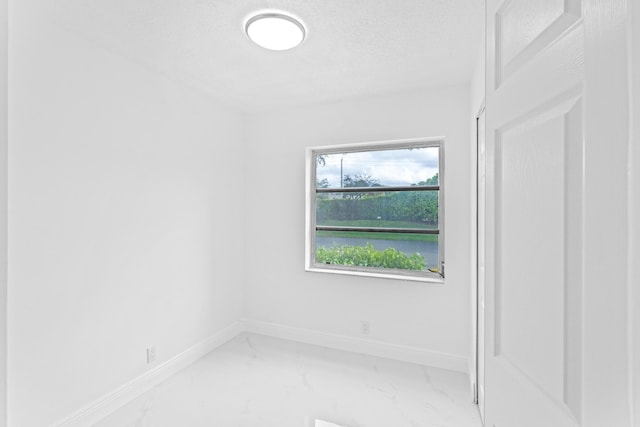 spare room with marble finish floor, baseboards, and a textured ceiling