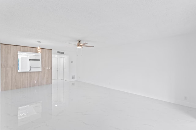 empty room with visible vents, a ceiling fan, marble finish floor, a textured ceiling, and wood walls