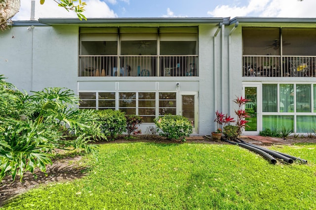 rear view of house featuring a yard, ceiling fan, and stucco siding