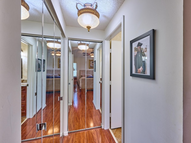 corridor with a textured ceiling and wood finished floors